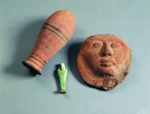 Tre egyptiske genstande, t.v. en dråbeformet flaske, højde 27 cm, 1400 f.Kr. Fladt leransigt, diameter 21 cm, 3.-2. årh. f.Kr. Lille grøn kvindefigur, en ushabti, ca. 1000-332 f.Kr., højde 12 cm.